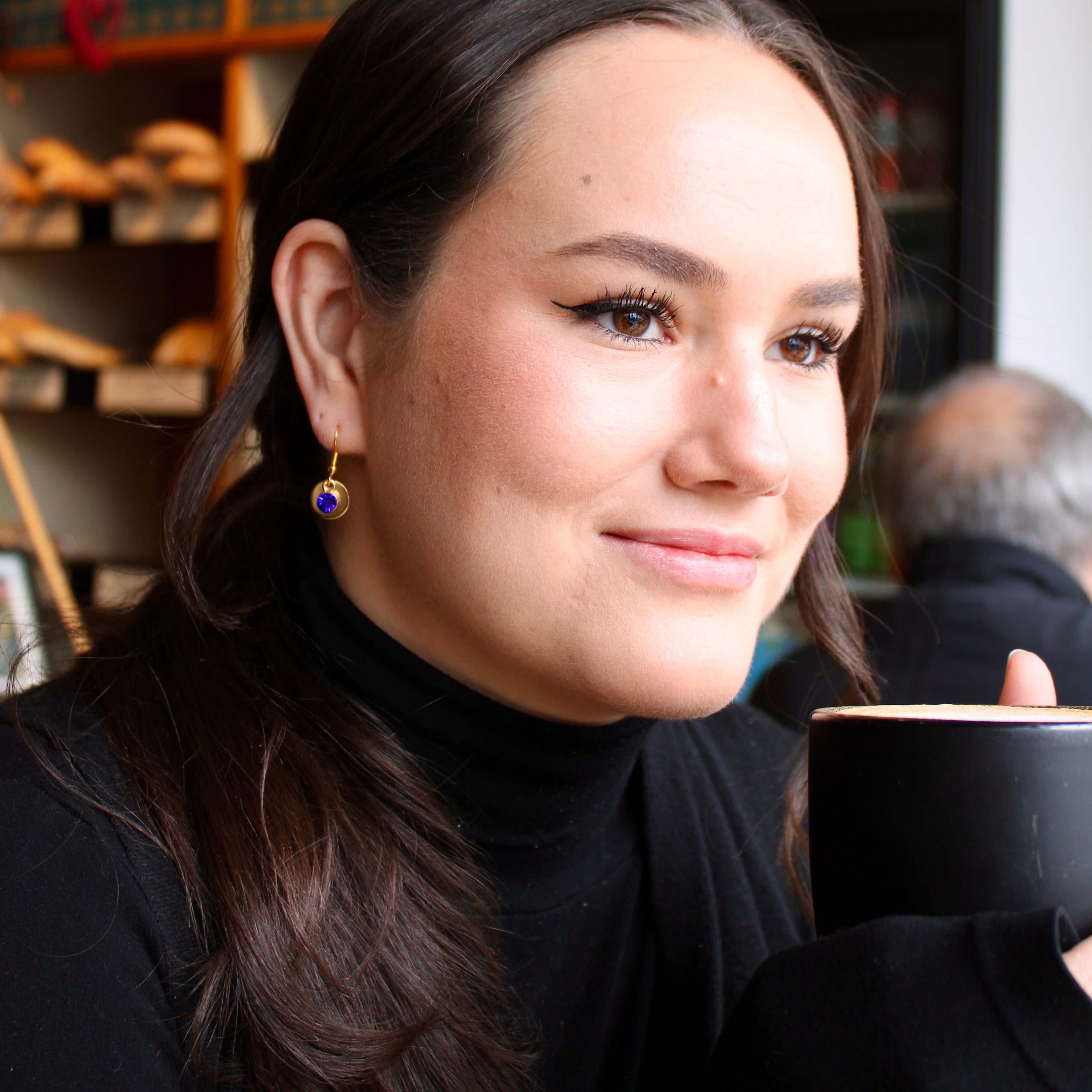 woman drinking coffee wearing blue hoop and gem earring